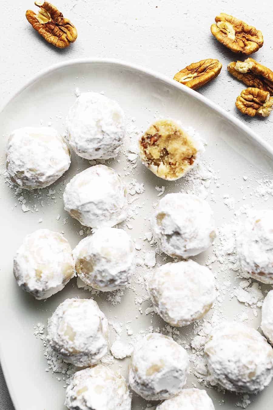 low carb sugar free snowball cookies arranged on a white platter with a sprinkle of nuts