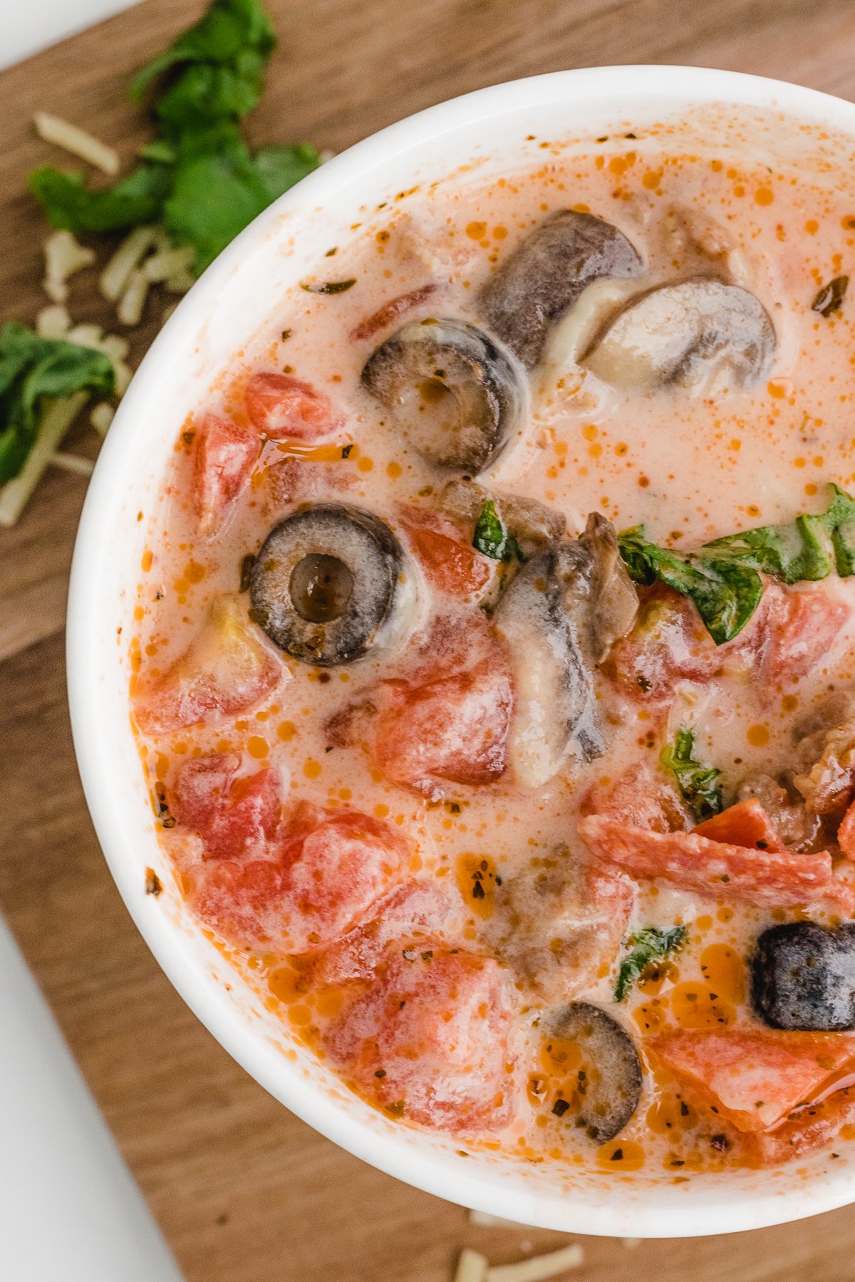 a close up of loaded pizza soup in a white bowl