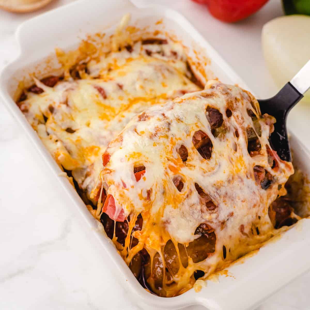 slow cooker sausage peppers and onions in a baking dish topped with cheese