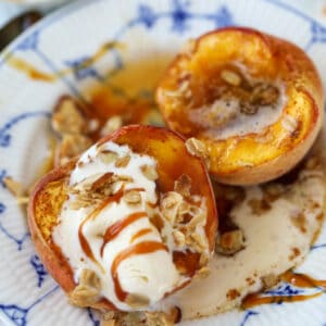 baked peaches recipe close up with toppings on a blue and white plate