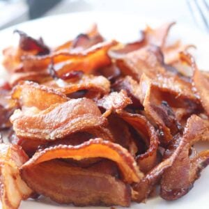 cooking bacon in air fryer on a white plate after it's done