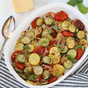 baked zucchini and squash with cheese in a white pan on a striped cloth background