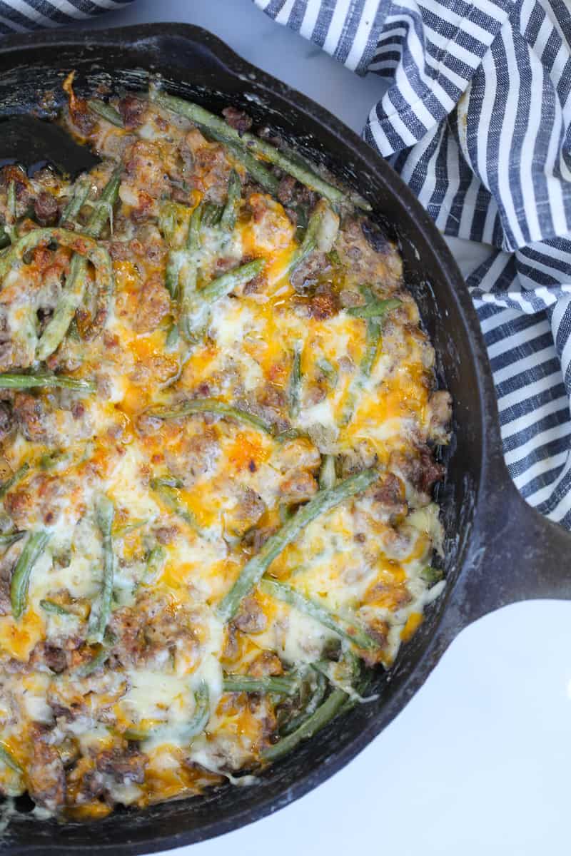 ground beef green bean casserole vertical image in a skillet with melted cheese on top sitting on a white background