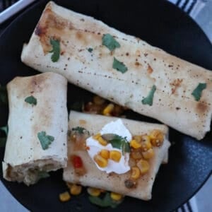 frozen burritos in air fryer on a plate after cooking with sour cream salsa and cilantro