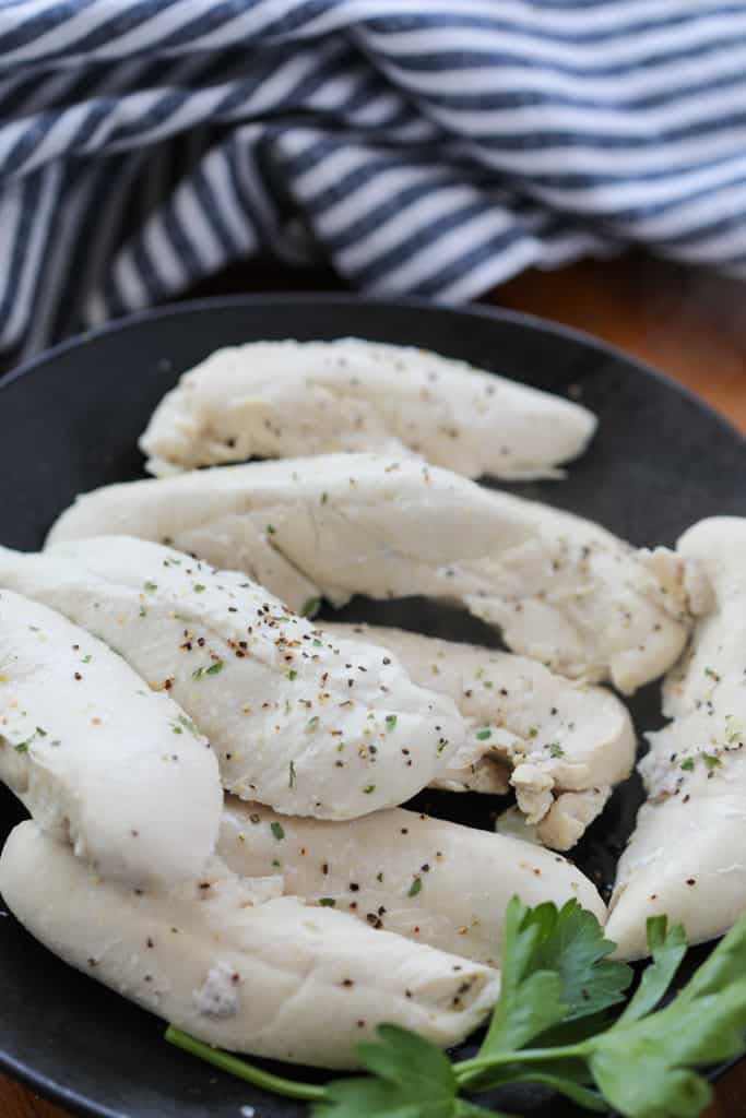 boiled chicken tenderloins on a black plate after simmering on the stovetop