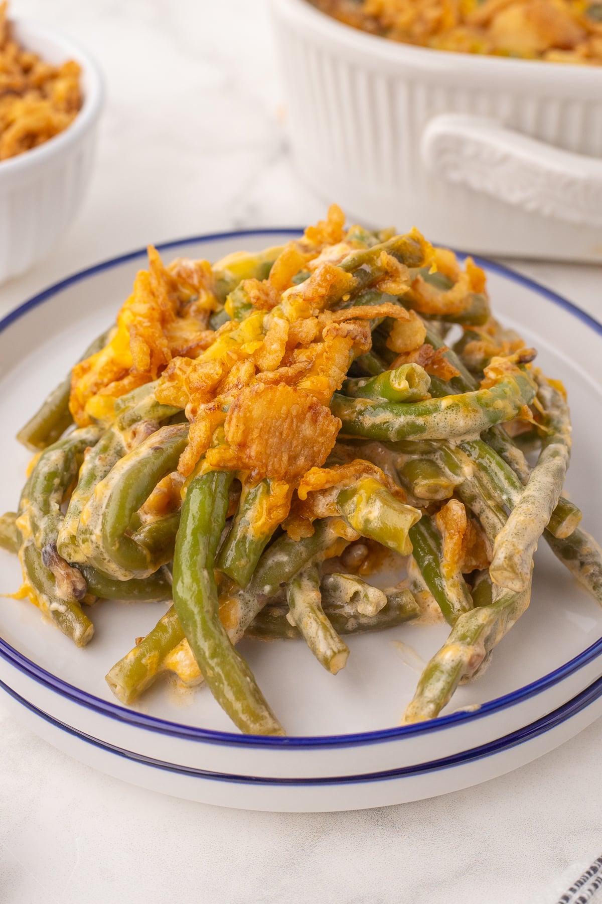 a white plate with a serving of green bean casserole with cream sauce, cheese, and fried onions on top