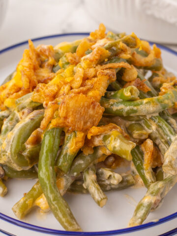 a plate of green bean casserole topped with a serving of cheddar cheese and crunchy fried onions