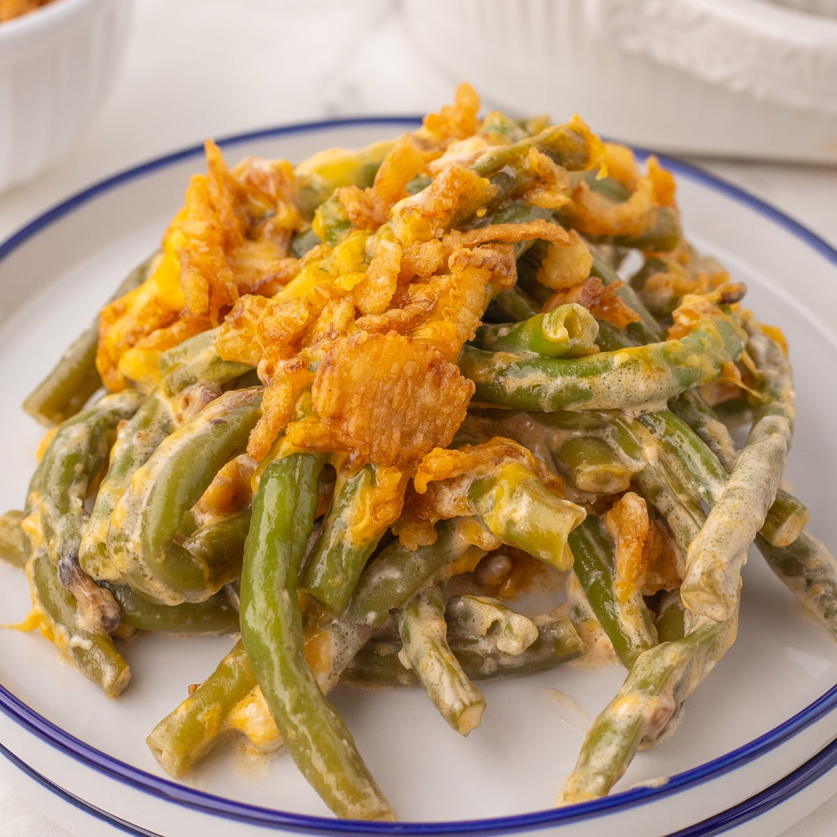 a plate of green bean casserole topped with a serving of cheddar cheese and crunchy fried onions