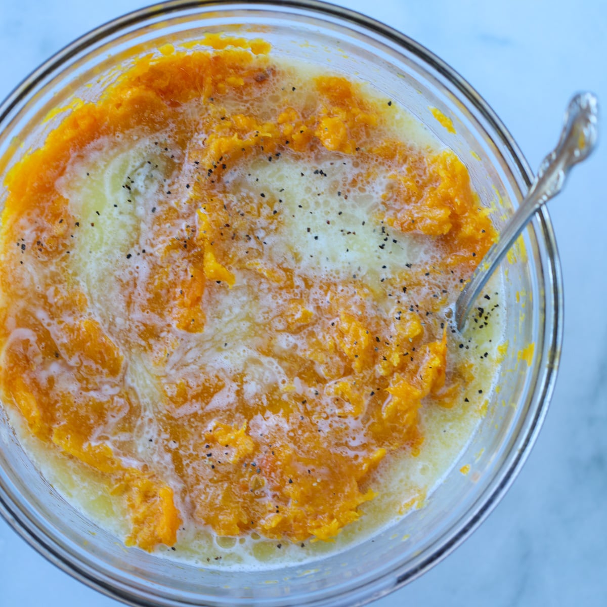 adding milk and butter to a bowl of mashed butternut squash