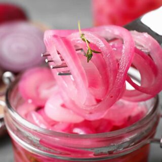 Pickled red onions being pulled from the jar with a fork.