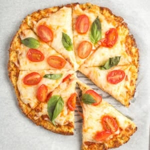 Cooked cauliflower pizza with a slice taken out.