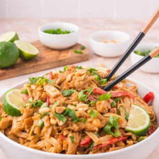 Garnished and served bowl of thai peanut noodles with chop sticks.