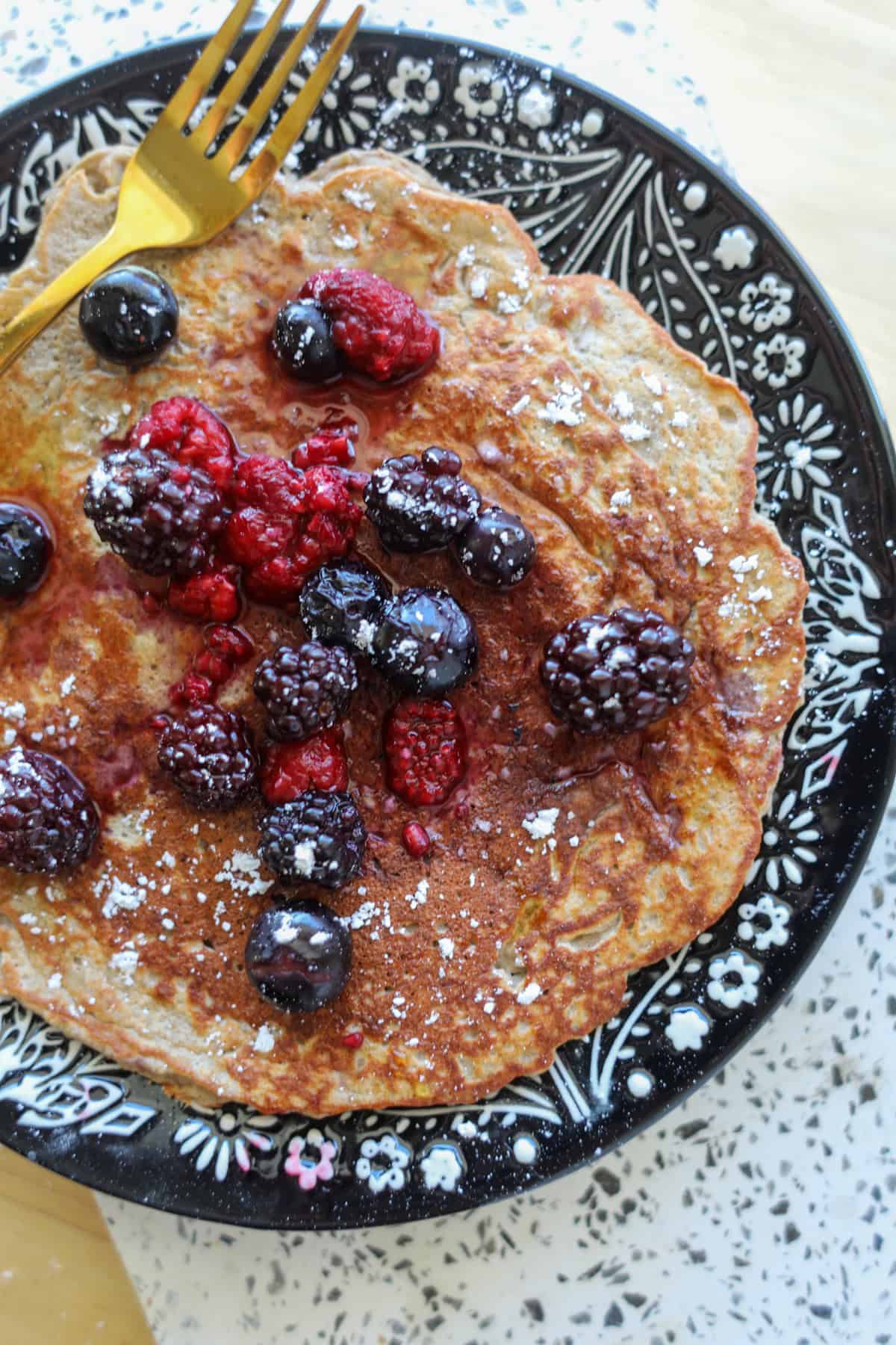 protein pancakes on a black plate sprinkled with berries and powdered sugar
