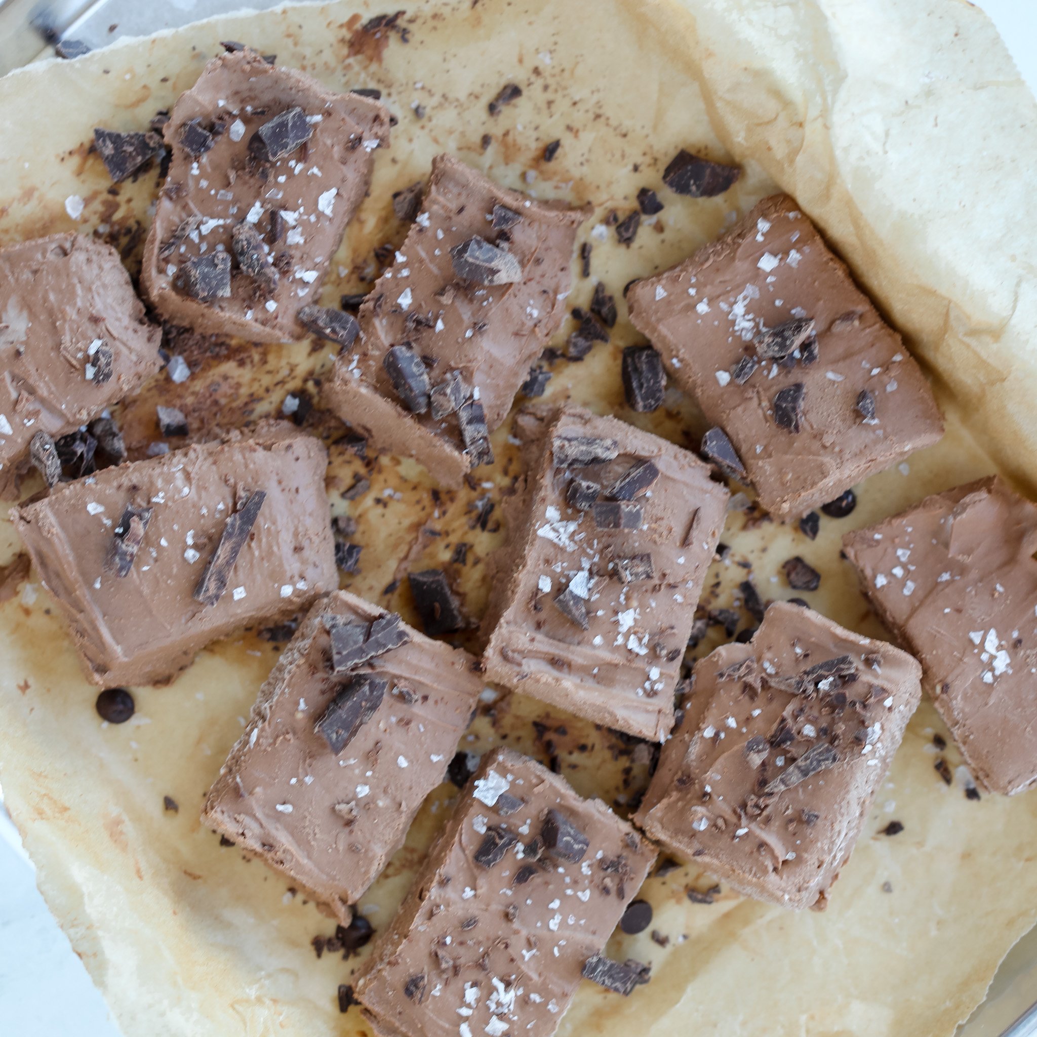 cottage cheese fudge cut up on parchment paper sprinkled with chopped dark chocolate and sea salt