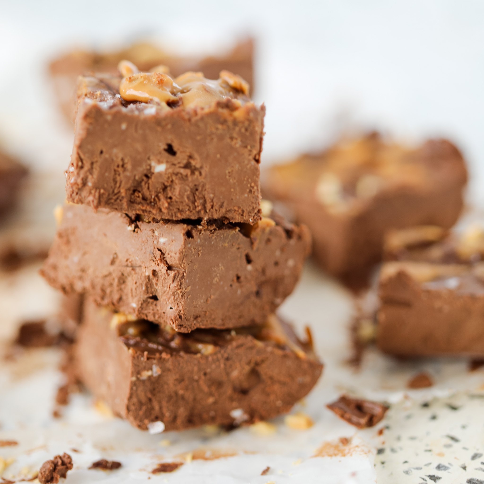 chocolate peanut butter cottage cheese fudge stacked up on a cutting board sprinkled with peanuts
