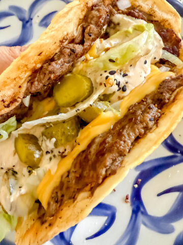 close up of a big mac smash burger taco coming off hot of the flattop griddle.
