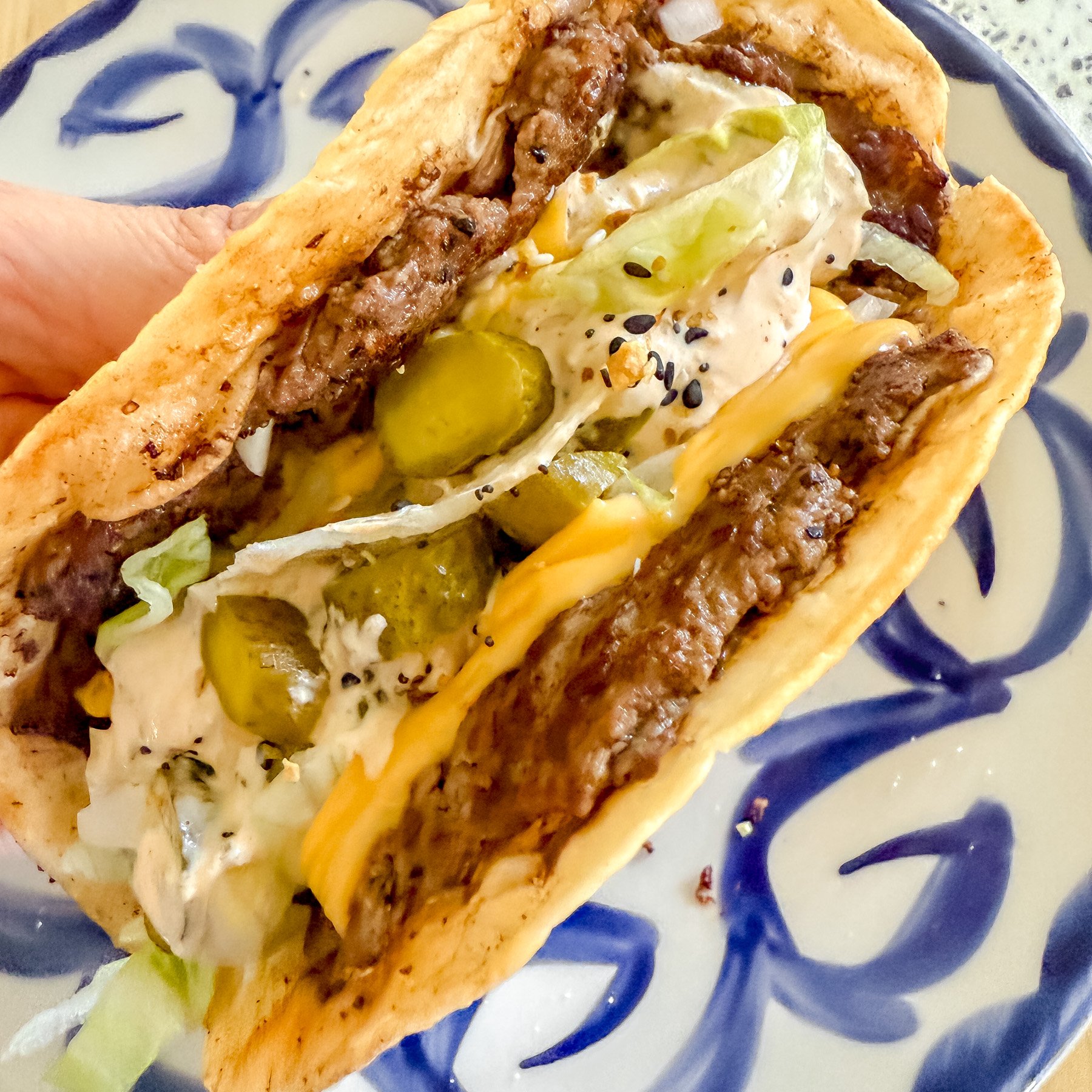 close up of a big mac smash burger taco coming off hot of the flattop griddle.