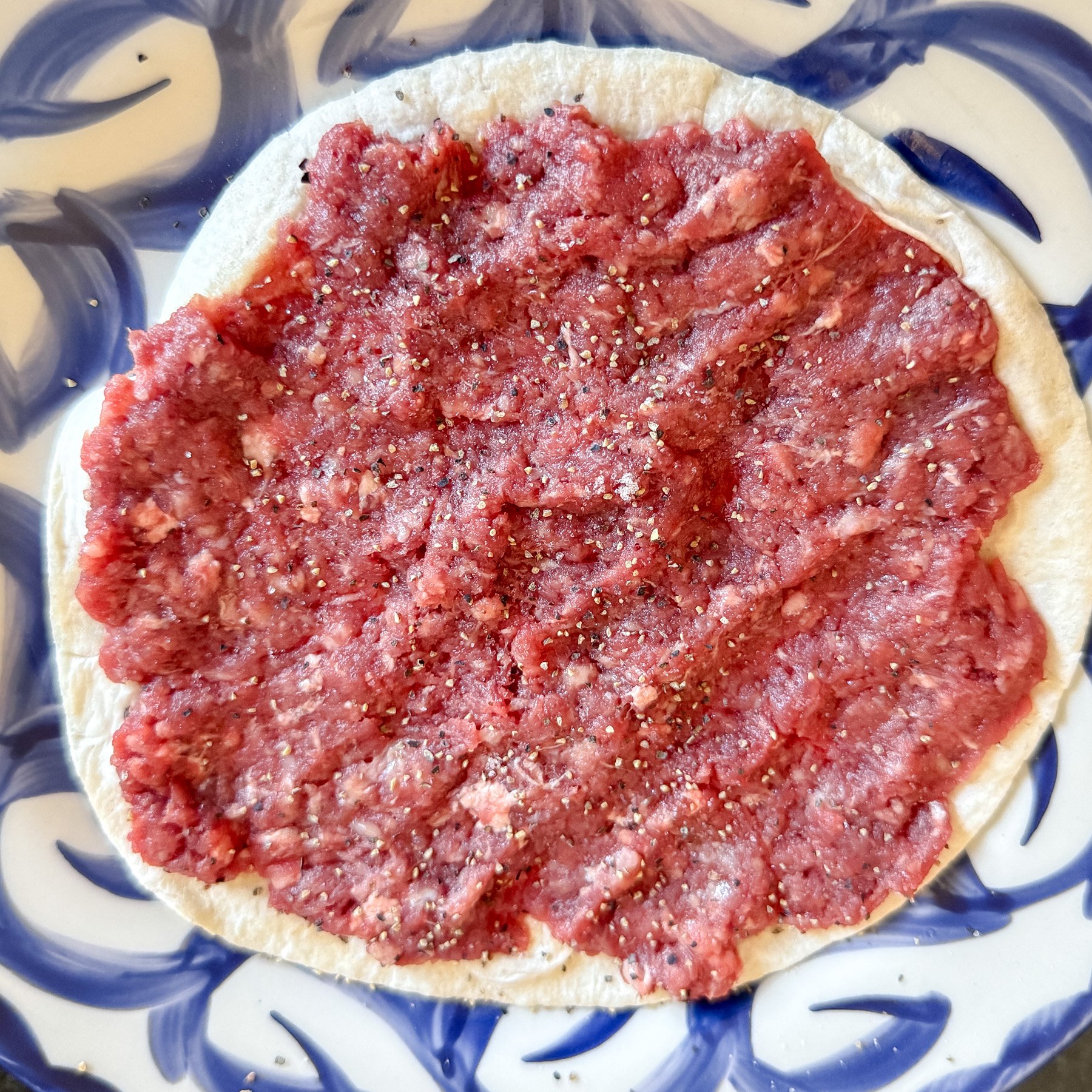 smashing the burgers on the tortillas on a plate or board