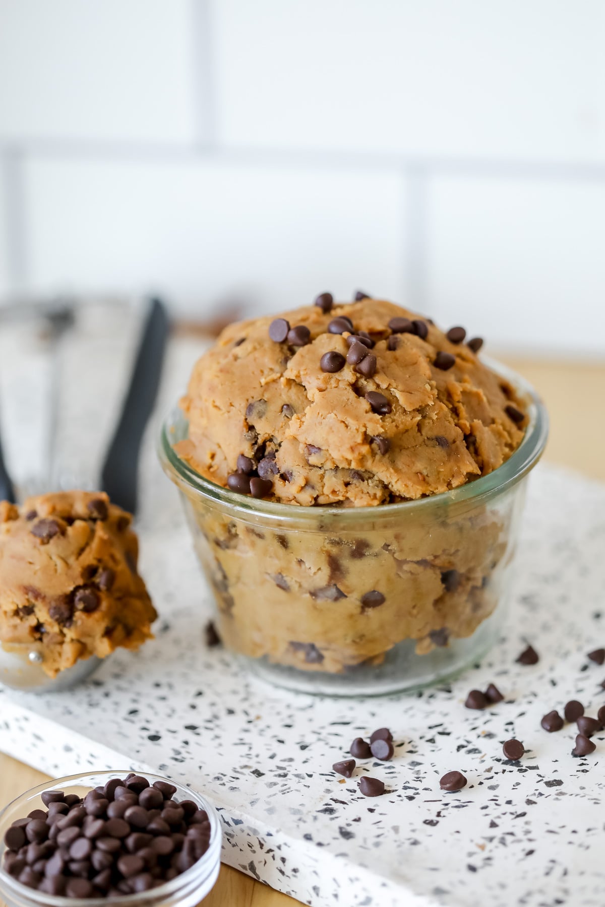 edible chocolate chip cookie dough made with chickpeas in a clear glass cup next to a spoonful of cookie dough.