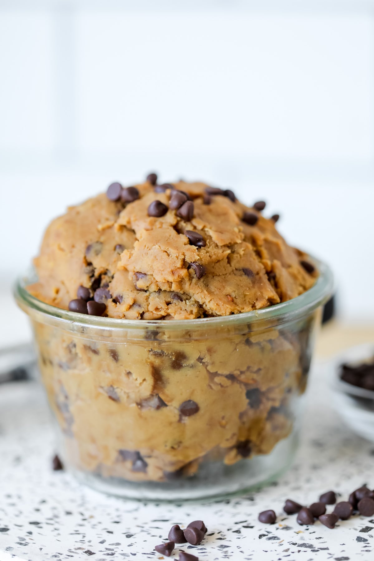 edible chickpea chocolate chip cookie dough on a white background next to a sprinkle of chocolate chips
