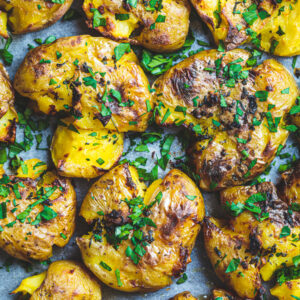smashed potatoes on the blackstone close up drizzled with garlic butter and chopped parsley