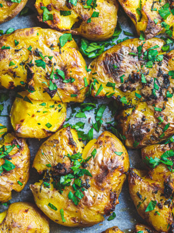smashed potatoes on the blackstone close up drizzled with garlic butter and chopped parsley