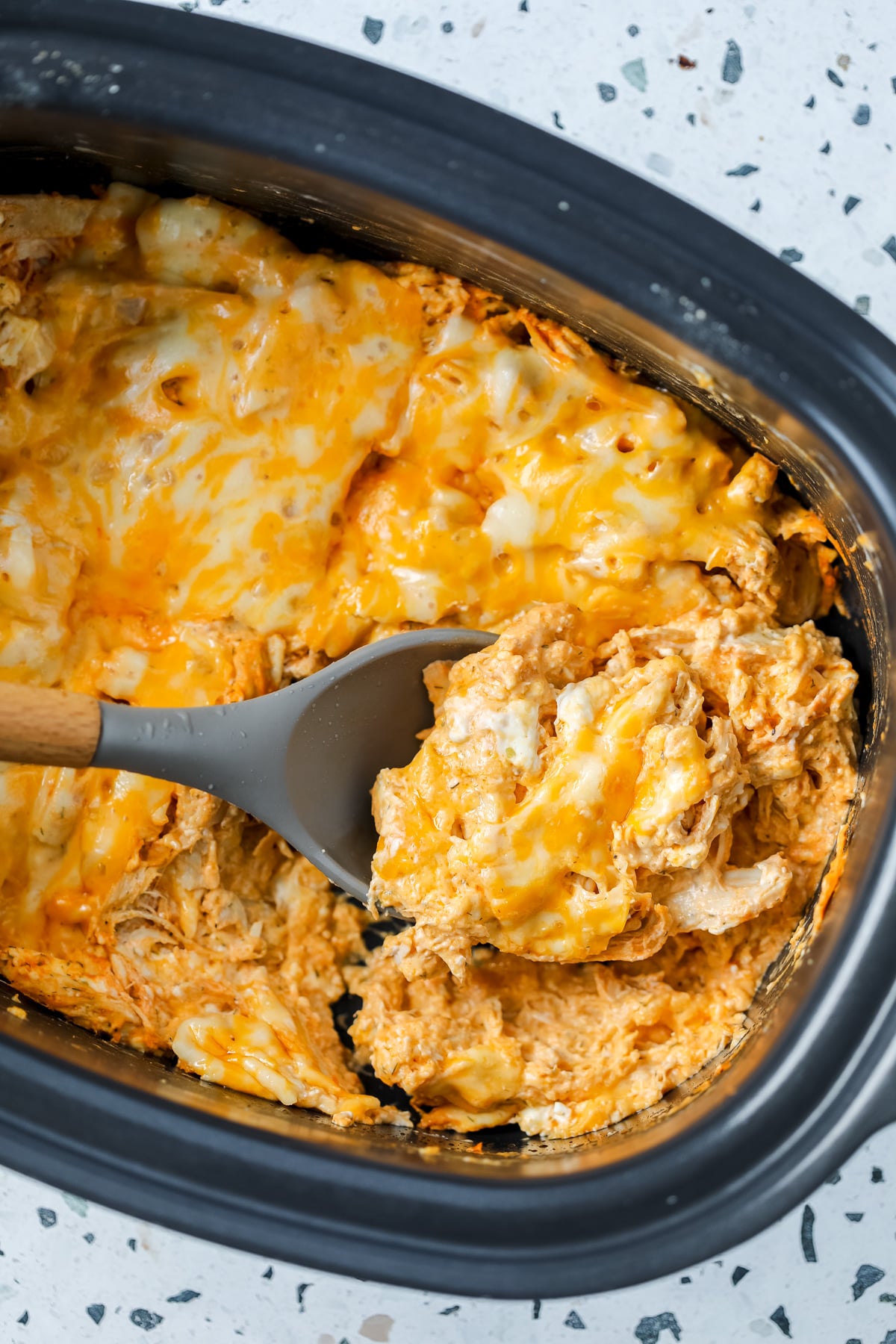 no carb crockpot buffalo chicken casserole topped with cheese and a black spoon dishing a scoop