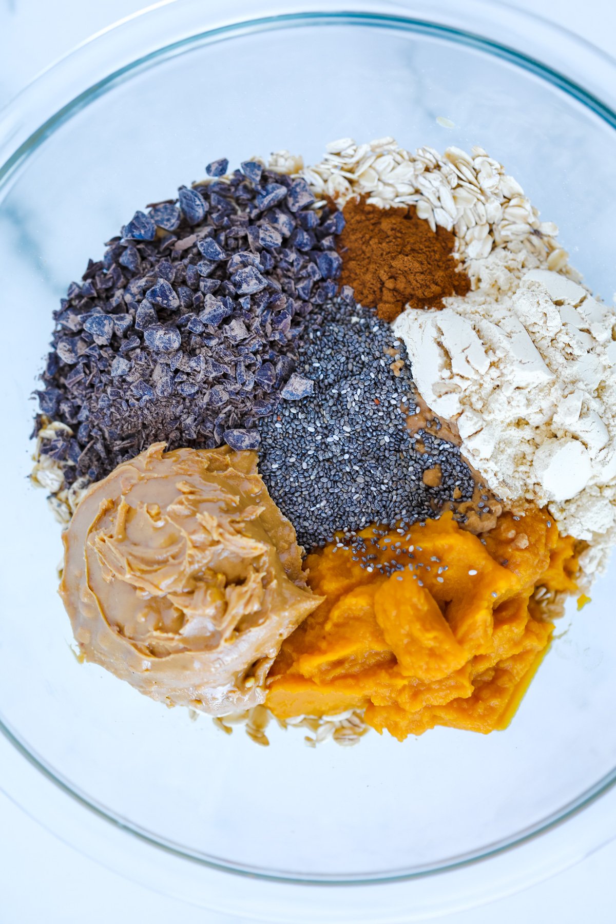 pumpkin spice protein balls ingredients in a mixing bowl including pumpkin chia seeds peanut butter chocolate chips and protein powder