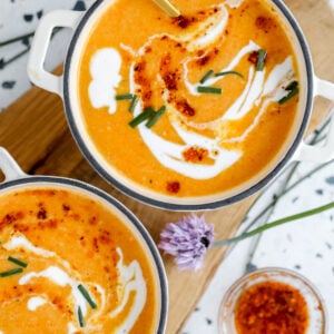 bowl of carrot soup with white swirls being served in a white bowl with a green lining