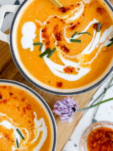 bowl of carrot soup with white swirls being served in a white bowl with a green lining
