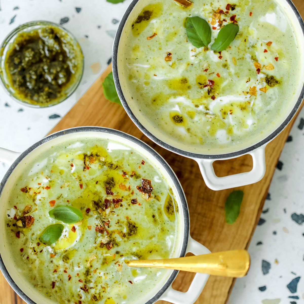 Two bowls of creamy zucchini soup being served on a wooden board