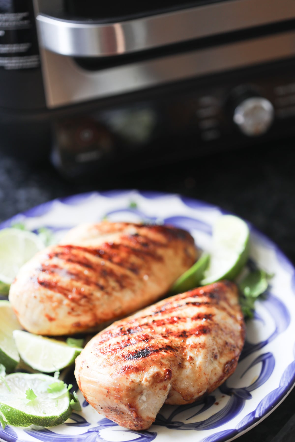 boneless skinless chicken breasts on a white plate after cooking on a ninja foodi grill